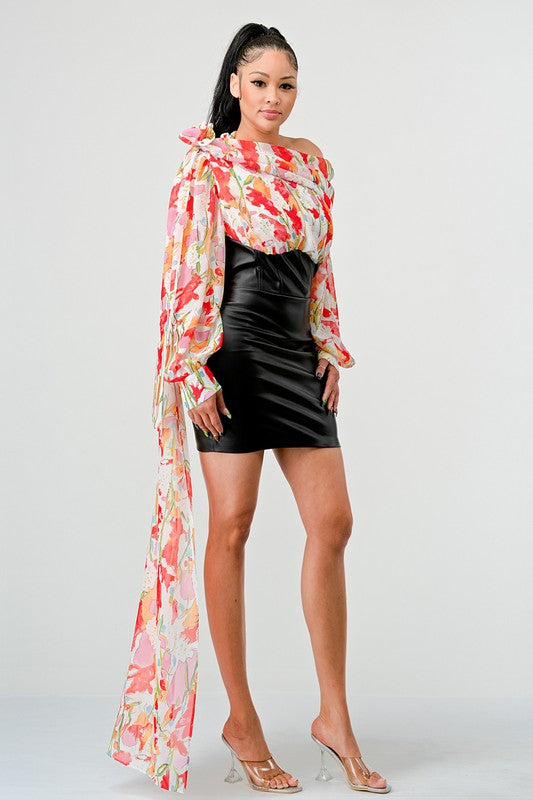 a woman in a black leather mini skirt and a floral print off-the-shoulder top with dramatic sleeves.