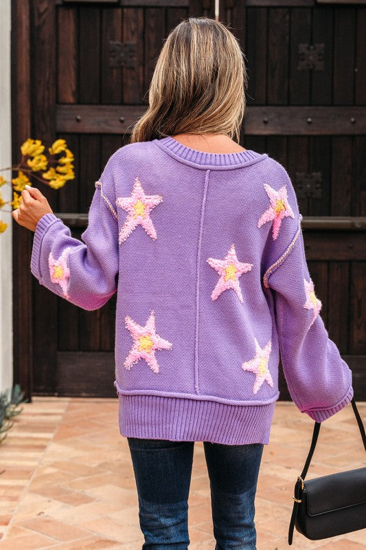 Woman wearing a purple oversized V-neck sweater with pink and yellow star patches, back view