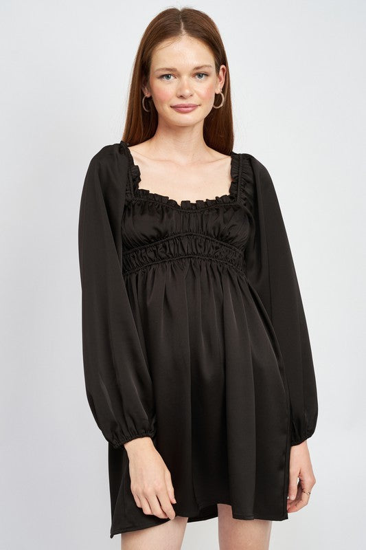 The dress is a black, long-sleeved mini with a smocked, square-neck bodice and a loose, flowy skirt that falls above the knees.