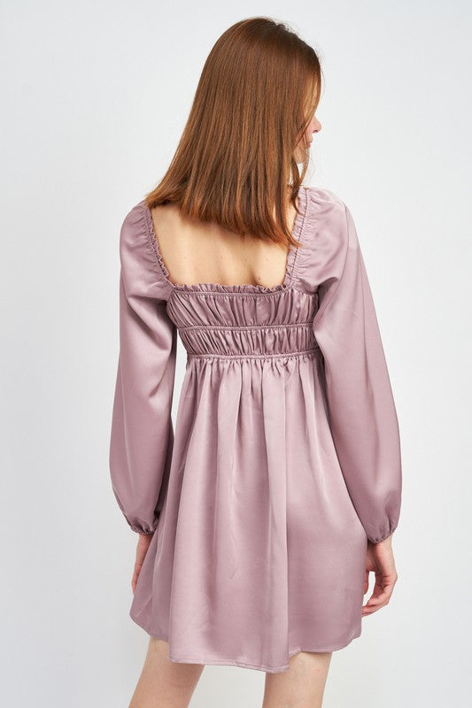 The dress is a puple, long-sleeved mini with a smocked, square-neck bodice and a loose, flowy skirt that falls above the knees.