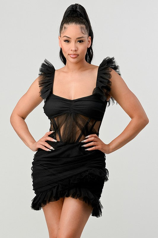 The dress is a chic black mini with a fitted silhouette, sheer paneling at the bodice, and dramatic ruffled cap sleeves that add a flirty, edgy touch