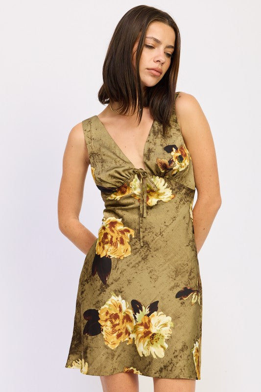 the dress is a short, olive-green floral wrap-style piece with a plunging neckline and a fitted silhouette, featuring large yellow and orange flowers.