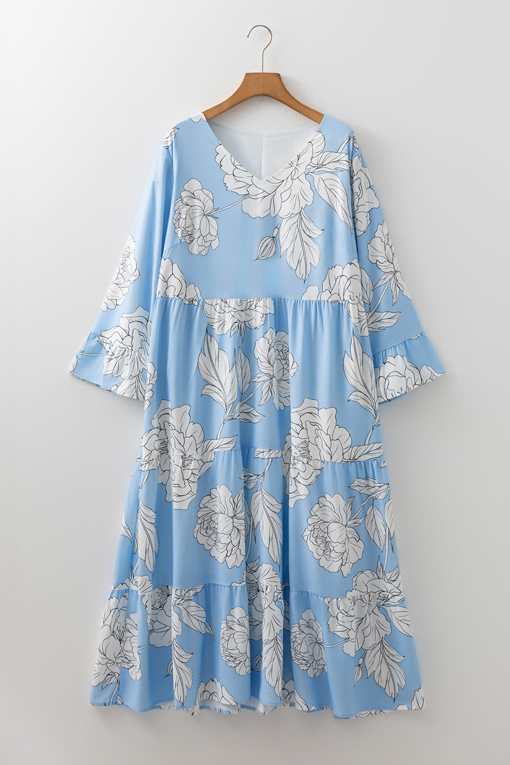 Woman in a sky blue floral maxi dress with white flowers, wearing a straw hat and sandals, holding a bouquet in a garden setting.