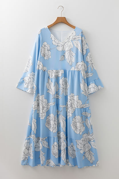 Woman in a sky blue floral maxi dress with white flowers, wearing a straw hat and sandals, holding a bouquet in a garden setting.