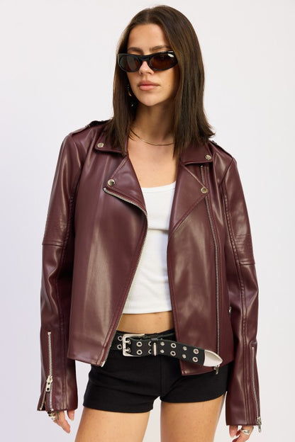Woman in burgundy leather jacket with white top and black shorts against beige background