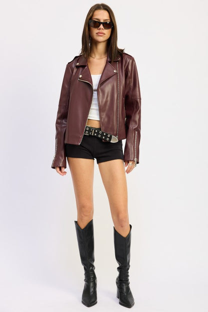 Woman in burgundy leather jacket and black outfit posing.