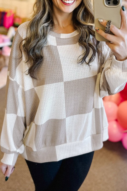 Person wearing a beige and white checkered sweater taking a mirror selfie.