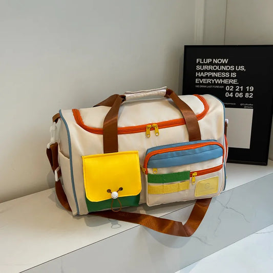White duffel bag with orange zippers and brown straps, featuring colorful external pockets in yellow, green, and blue. Playful and functional design—perfect for travel, gym, or casual outings.