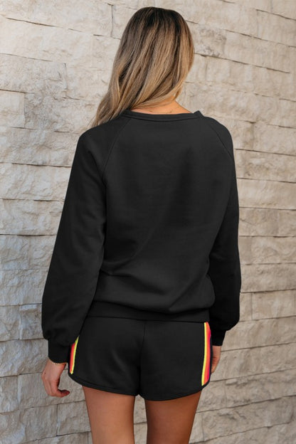 Person wearing a black sweatshirt and shorts with colorful trim against a stone wall.