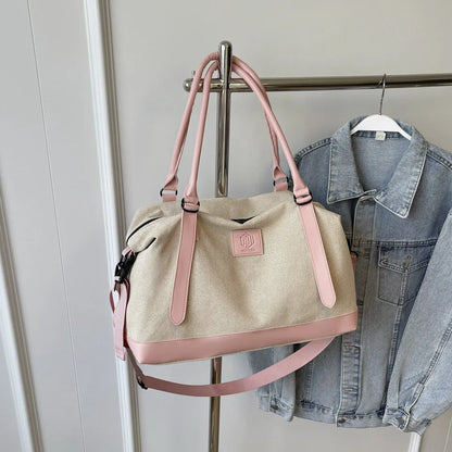 Beige and pink handbag with pink handles, base, shoulder strap, and front logo patch—hanging on a metal rack beside a light blue denim jacket in an indoor setting.