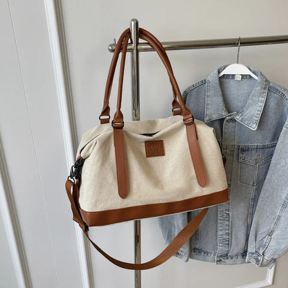Beige and brown handbag with leather handles, shoulder strap, and vertical accents—hanging beside a denim jacket on a metal rack against a white paneled wall.