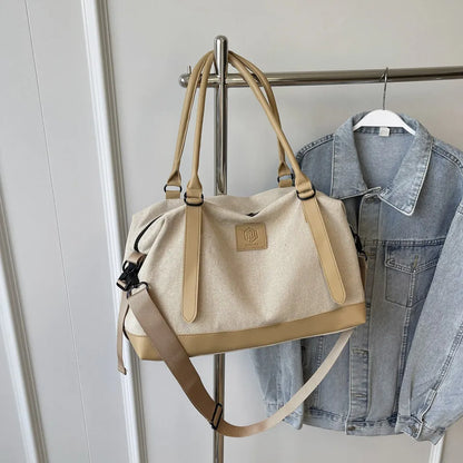 Beige and tan handbag with top handles, detachable shoulder strap, and front logo patch—hanging beside a denim jacket on a metal rack in a clean indoor setting.