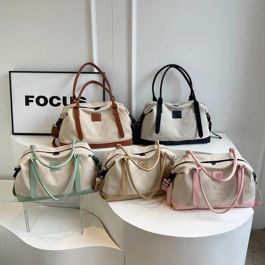 Five canvas handbags in varied colors—brown, black, mint green, mustard yellow, and pink—neatly displayed with matching handles and logo patches in a minimalist setting.