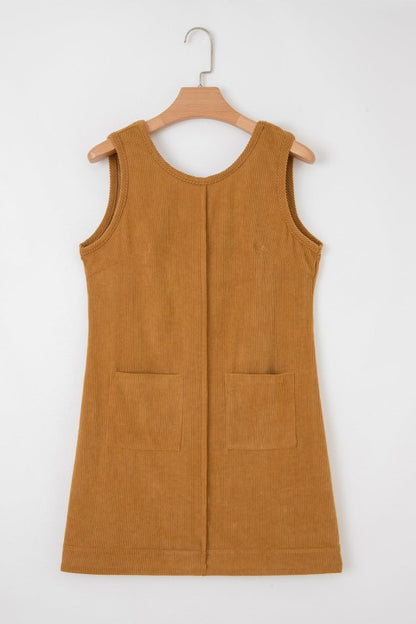 A brown corduroy sleeveless mini dress with front patch pockets, styled over a black lace long-sleeve top and paired with tan knee-high boots