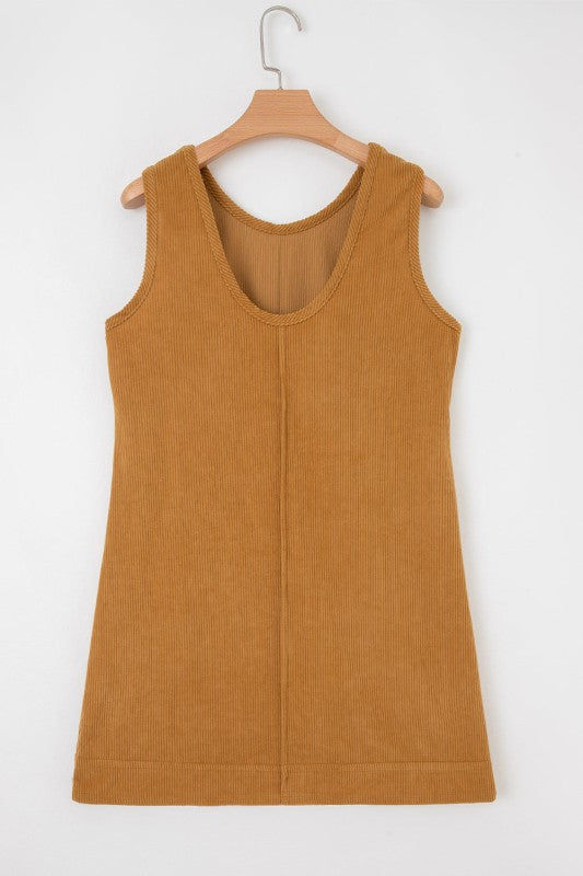 A brown corduroy sleeveless mini dress with front patch pockets, styled over a black lace long-sleeve top and paired with tan knee-high boots.