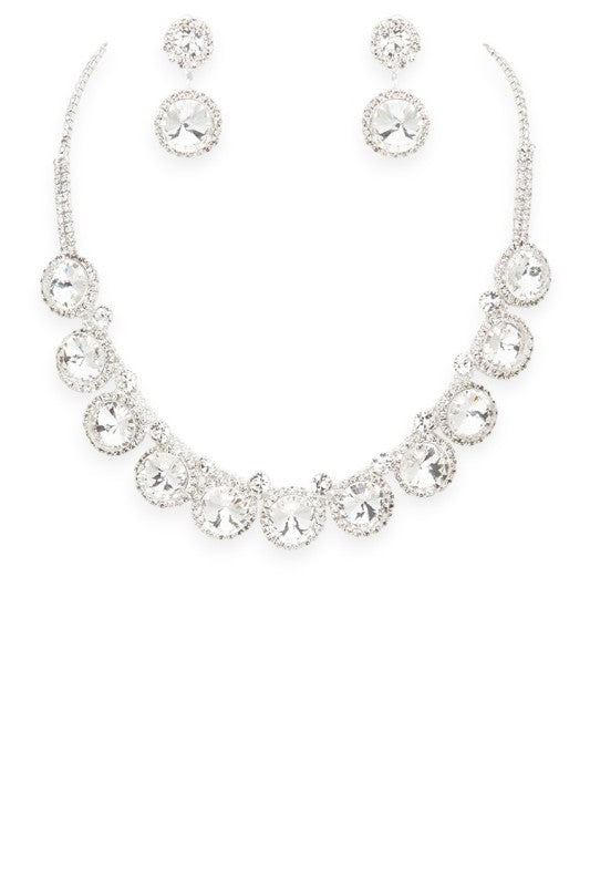 Lovely jewelry set featuring a silver-toned necklace and matching earrings, each adorned with large round clear gemstones surrounded by smaller stones, luxurious, symmetrical, and ideal for formal occasions.