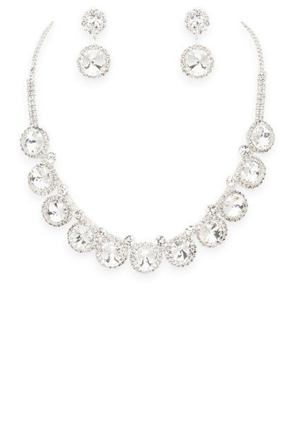 Lovely jewelry set featuring a silver-toned necklace and matching earrings, each adorned with large round clear gemstones surrounded by smaller stones, luxurious, symmetrical, and ideal for formal occasions.