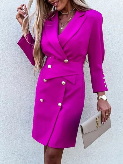 A woman in a stylish pink double-breasted blazer dress with gold buttons, accessorized with jewelry and a clutch. 