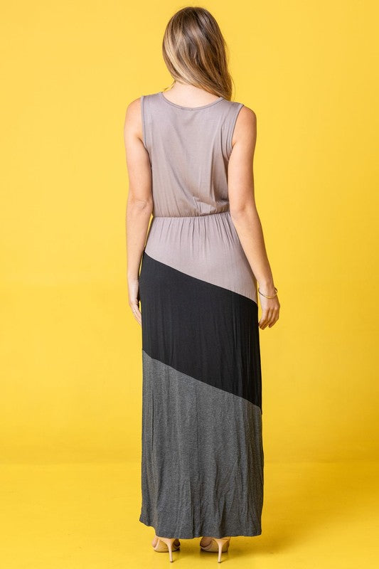 Woman in a colorblock maxi dress with gray top, black middle, and gray bottom sections. She's wearing strappy heels, standing against a bright yellow background.