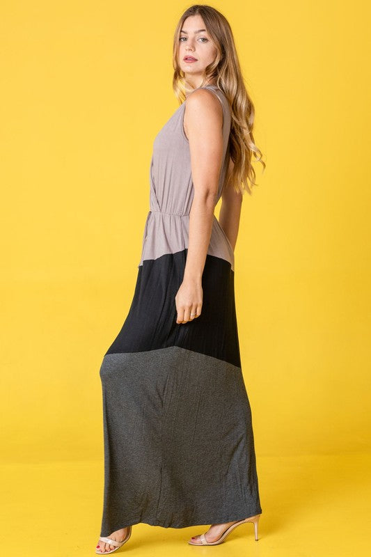 Woman in a colorblock maxi dress with gray top, black middle, and gray bottom sections. She's wearing strappy heels, standing against a bright yellow background.