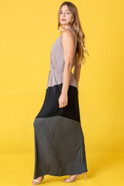 Woman in a colorblock maxi dress with gray top, black middle, and gray bottom sections. She's wearing strappy heels, standing against a bright yellow background.