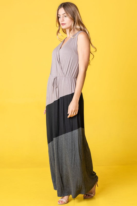 Woman in a colorblock maxi dress with gray top, black middle, and gray bottom sections. She's wearing strappy heels, standing against a bright yellow background.