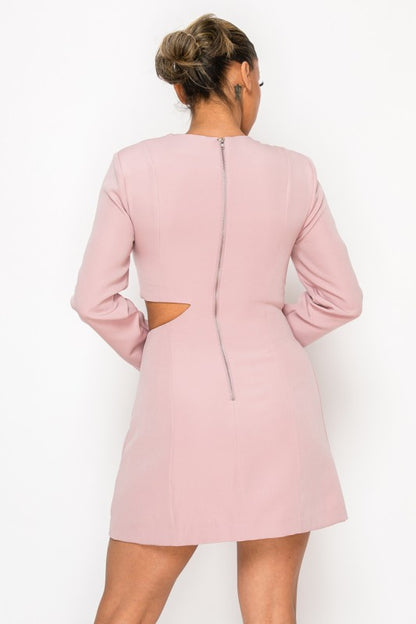 Woman wearing a long-sleeve mini dress with asymmetrical cutouts across the chest and midriff, styled against a plain white background.
