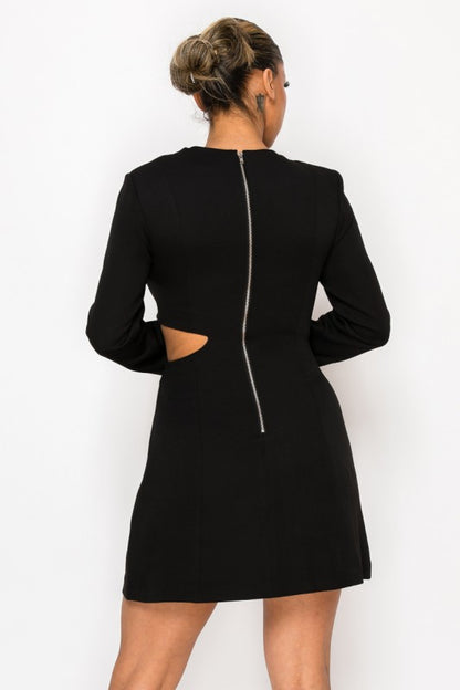 Woman wearing a long-sleeve mini dress with asymmetrical cutouts across the chest and midriff, styled against a plain white background.