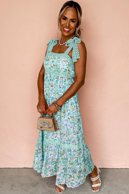 Woman wearing a turquoise floral maxi dress with tie straps, standing in front of tropical plants on gravel.
