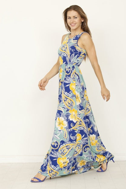 A woman posing in a long, sleeveless blue dress with a vibrant yellow floral pattern. 