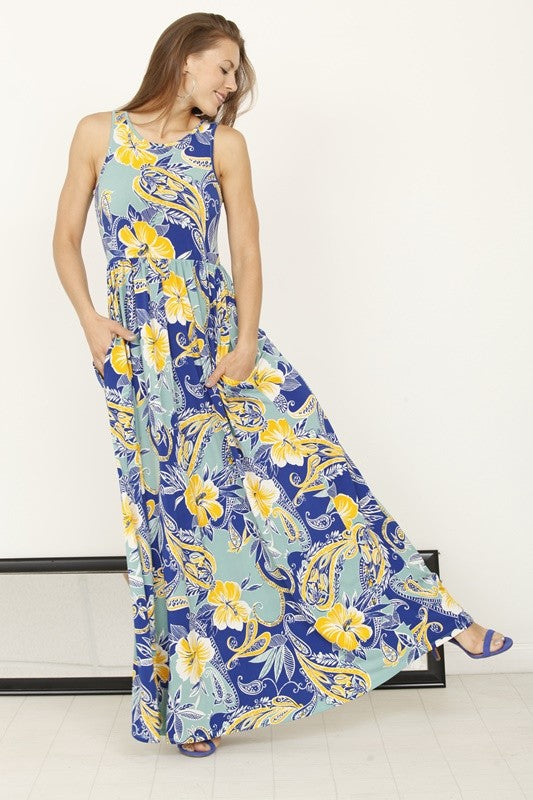 A woman posing in a long, sleeveless blue dress with a vibrant yellow floral pattern. 