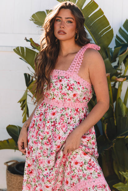 Woman wearing a pink floral maxi dress with lace-trimmed straps, posing in front of tropical plants on gravel.