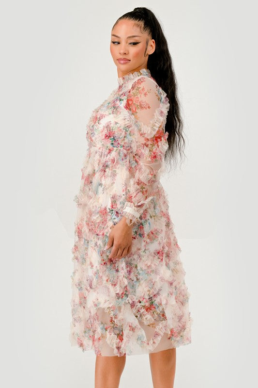 A woman models a Floral Ruffle Sheer Midi Dress, features an all over pastel floral print with cascading ruffle detailing for a soft, textured finish. 