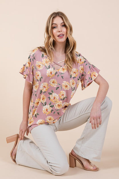 Woman in floral top with yellow flowers and beige pants on neutral background