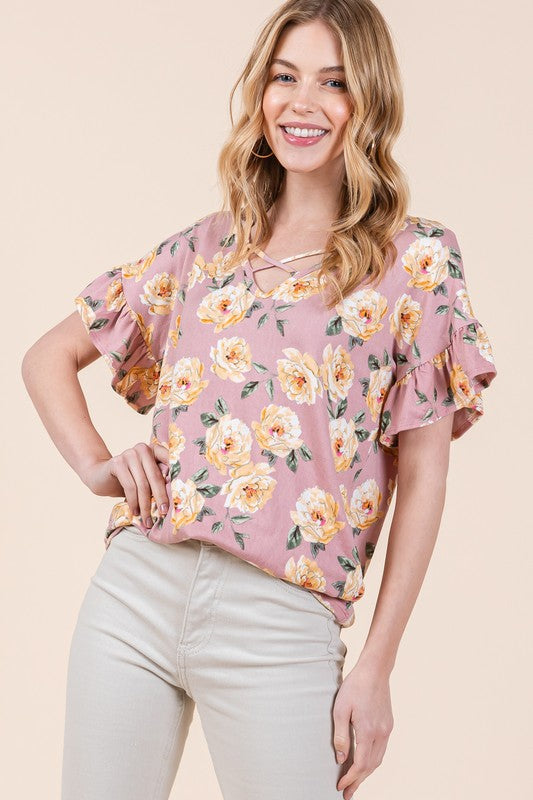 Woman wearing pink floral shirt with yellow blooms and beige trousers against neutral backdrop"