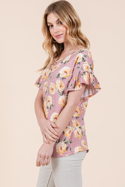 Woman dressed in pink floral shirt featuring yellow flowers and beige pants on neutral setting