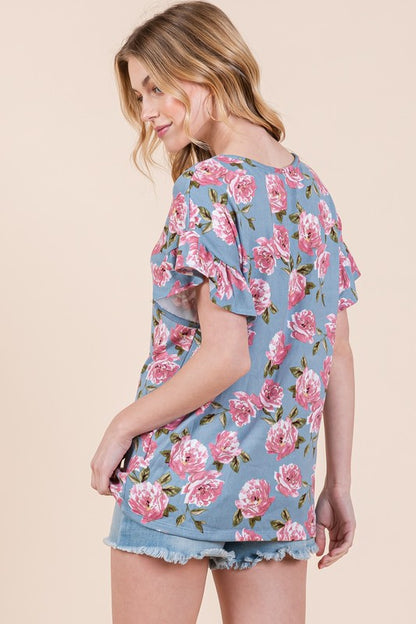 Back view of a woman in blue floral top with denim shorts against beige background