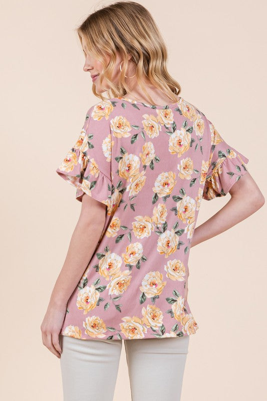 Woman sporting pink floral blouse with yellow blooms and beige bottoms on neutral backdrop