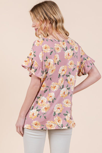 Woman sporting pink floral blouse with yellow blooms and beige bottoms on neutral backdrop