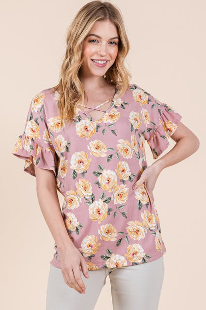 Woman in pink flower-print blouse with yellow florals and beige slacks on neutral background