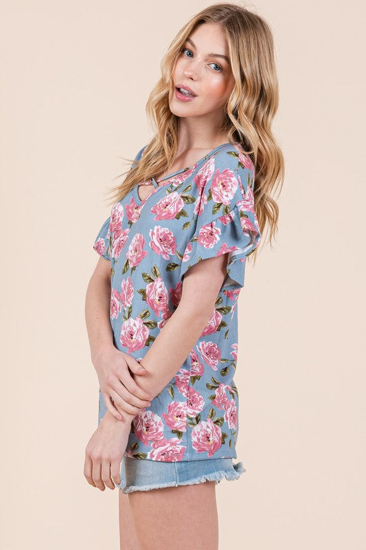 Side view of Woman wearing pink floral blue top with denim shorts against beige background