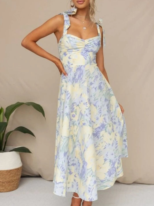 Woman models a charming floral midi dress with tie-shoulder straps, a ruched bust, and a flowing skirt, ideal for summer.