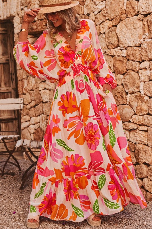 A woman wearing a flowy maxi dress with a vibrant floral print in pink, orange, and green.
