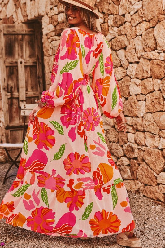 A woman wearing a flowy maxi dress with a vibrant floral print in pink, orange, and green