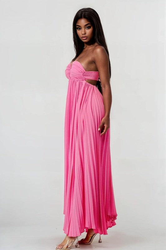 The image shows a woman with dark skin and long black hair wearing a hot pink, strapless maxi dress with a pleated skirt and a sweetheart neckline.