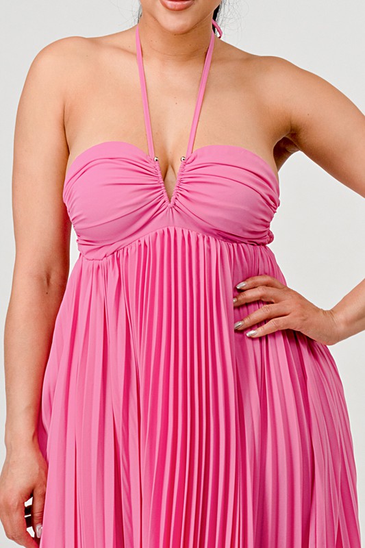 The image shows a woman with dark skin and long black hair wearing a hot pink, strapless maxi dress with a pleated skirt and a sweetheart neckline.