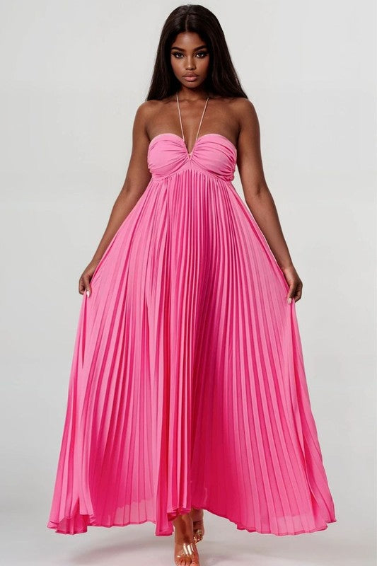 The image shows a woman with dark skin and long black hair wearing a hot pink, strapless maxi dress with a pleated skirt and a sweetheart neckline.