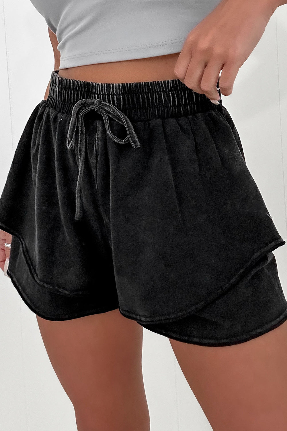 A person wearing black mineral wash French terry shorts with an elastic waistband and drawstring, paired with a white crop top. The shorts look soft, comfortable, and ideal for casual wear, lounging, or street style