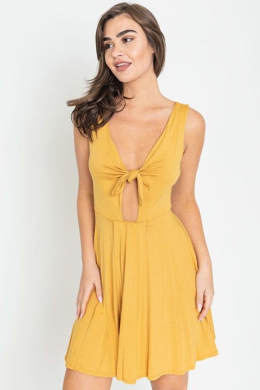 Woman in a mustard yellow sleeveless mini dress with a front knot, deep V-neckline, and cut-out detail below the bust.
