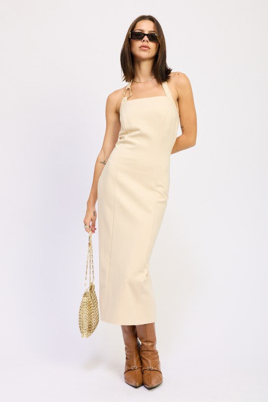 Woman models a chic halter neck midi dress in a neutral cream color, featuring a fitted silhouette and elegant design.